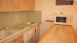 A compact kitchen with wooden cabinets, a dishwasher, a microwave, and a small countertop.
