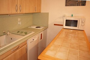 A compact kitchen with wooden cabinets, a built-in dishwasher, a microwave, and a small countertop with a green mat.