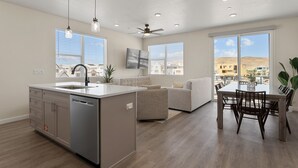 Eine moderne Küche mit einer zentralen Kochinsel, einem Essbereich mit Tisch und Stühlen, einem Deckenventilator und großen Fenstern mit Blick auf die Stadt.