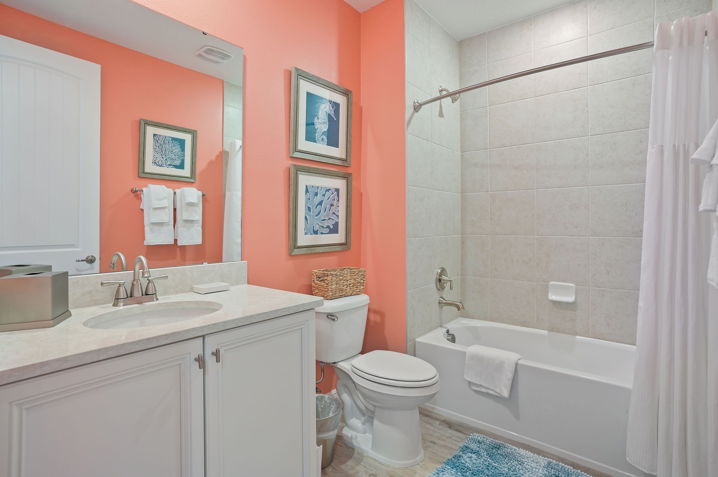 A bathroom with a white sink, toilet, and bathtub. There are framed pictures on the wall and a towel rack.
