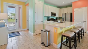 A modern kitchen with white cabinets, a stainless steel refrigerator, and a large island with bar stools. - Surfstyle At Margaritaville By Shine Villas 022 3 Bedroom Villa (Kissimmee)