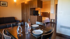 Et moderne hotelværelse med et træspisebord dækket til to personer, en sofa, et fjernsyn og en seng.