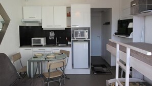 Eine kompakte Küche mit weißen Schränken, einer Mikrowelle, einem Kühlschrank und einem Esstisch mit Stühlen.