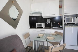 A compact kitchen with white cabinets, a microwave, a toaster, and a refrigerator.