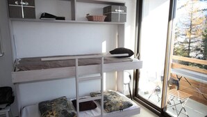 Ein Stockbett mit Stauraumschränken, ein Fenster mit Blick auf Bäume und ein Stuhl draußen.