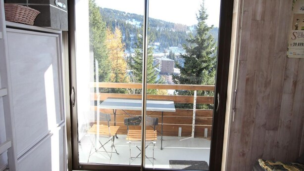 Ein Zimmer mit einer Schiebeglastür, die auf einen Außenbalkon mit einem Holztisch und Stühlen führt.