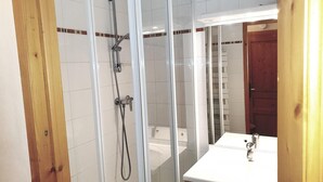 A bathroom with a glass shower enclosure, a white sink, and a wooden door. - 150m from ski slopes, 5th floor, view resort, balcony, tv, 55m², Méribel (Méribel - Les Allues)