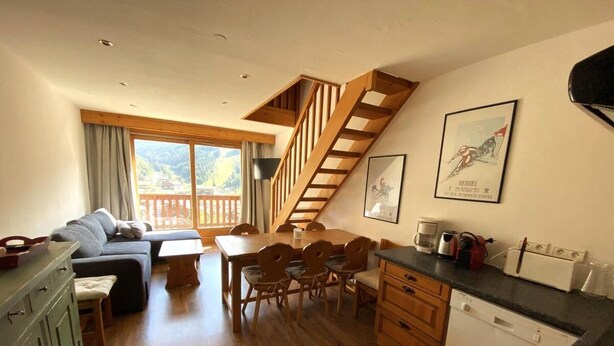 A cozy living room with a sofa, a dining table with chairs, a staircase, and a kitchen area with a dishwasher. - 150m from ski slopes, 5th floor, view resort, balcony, tv, 55m², Méribel (Méribel - Les Allues)