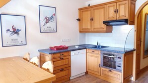 A kitchen with wooden cabinets, a dishwasher, an oven, and a microwave. There are two framed pictures on the wall. - 150m from ski slopes, 5th floor, view resort, balcony, tv, 55m², Méribel (Méribel - Les Allues)