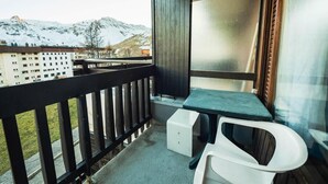 A balcony with a view of snow-capped mountains, a wooden railing, a small table, and a white chair.