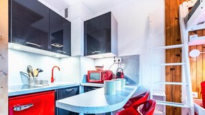 A compact kitchen with a red refrigerator, a microwave, and a sink. There are two red chairs and a white ladder.