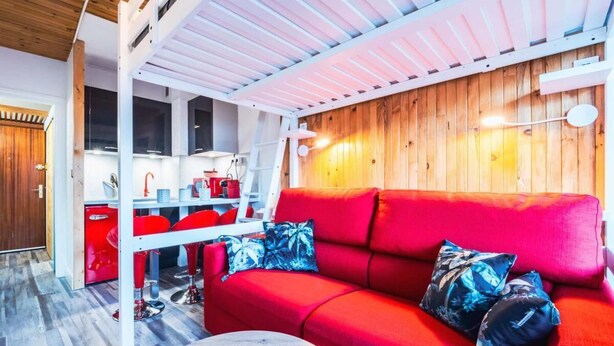 A compact living space with a red sofa, a dining area with red chairs, and a kitchen area.