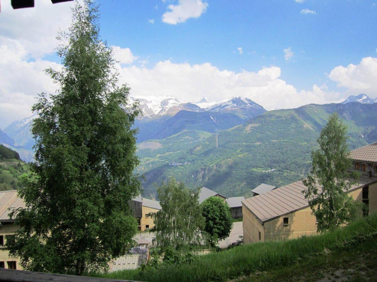 Un borgo montano con case tradizionali e una vista chiara di cime innevate sullo sfondo.
