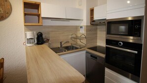 Eine kleine Küche mit weißen Schränken, einer Holz Arbeitsplatte, einer Kaffeemaschine, einem Spülbecken und einem eingebauten Backofen.
