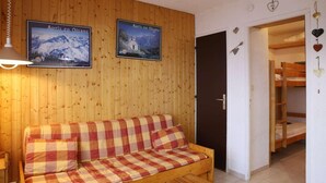 Ein Holzinnenraum mit einer Couch, Postern, einer Tür und einem Etagenbett.