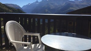 Ein Balkon mit weißem Plastikstuhl und rundem Tisch, mit Blick auf eine gebirgige Landschaft.