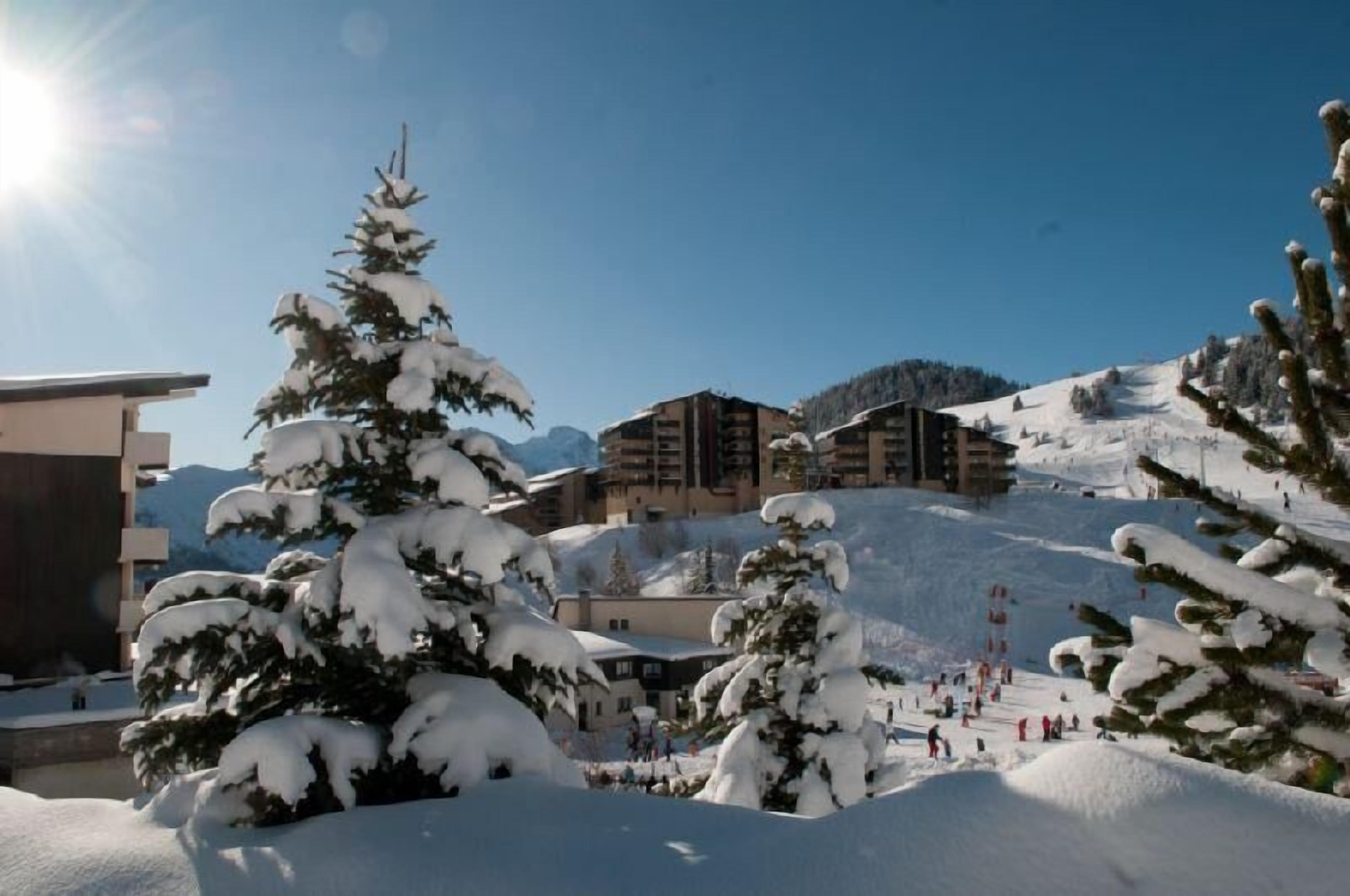 Une station de ski enneigée, avec des bâtiments et des arbres.
