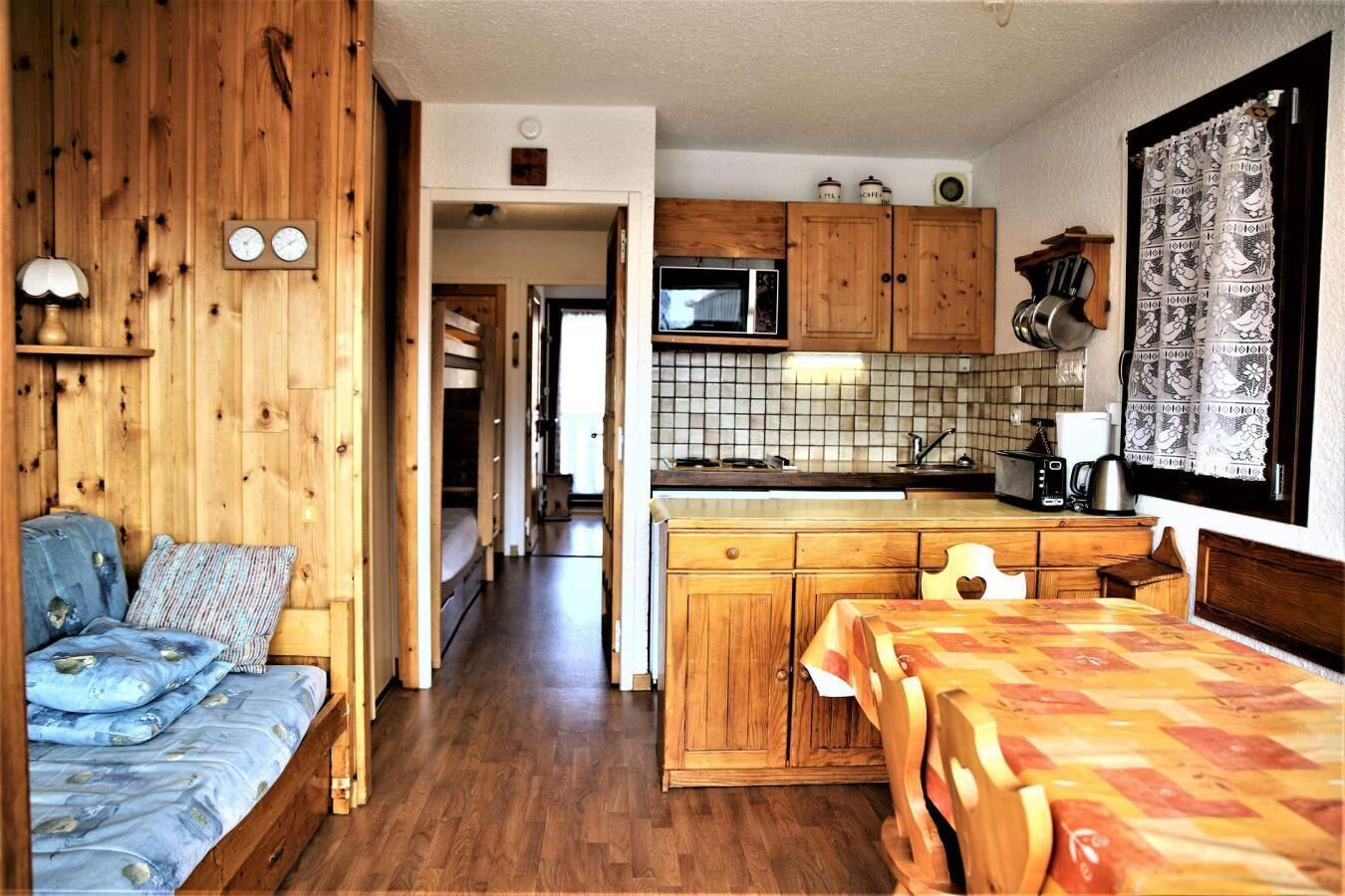 Eine kleine Küche mit Holzausstattung, einer Mikrowelle und einem Spülbecken. Es gibt einen kleinen Essbereich mit Tisch und Stühlen.