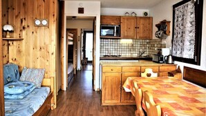 Una cocina compacta con armarios de madera, microondas y un lavamanos. Hay una pequeña zona de comedor con una mesa y sillas.
