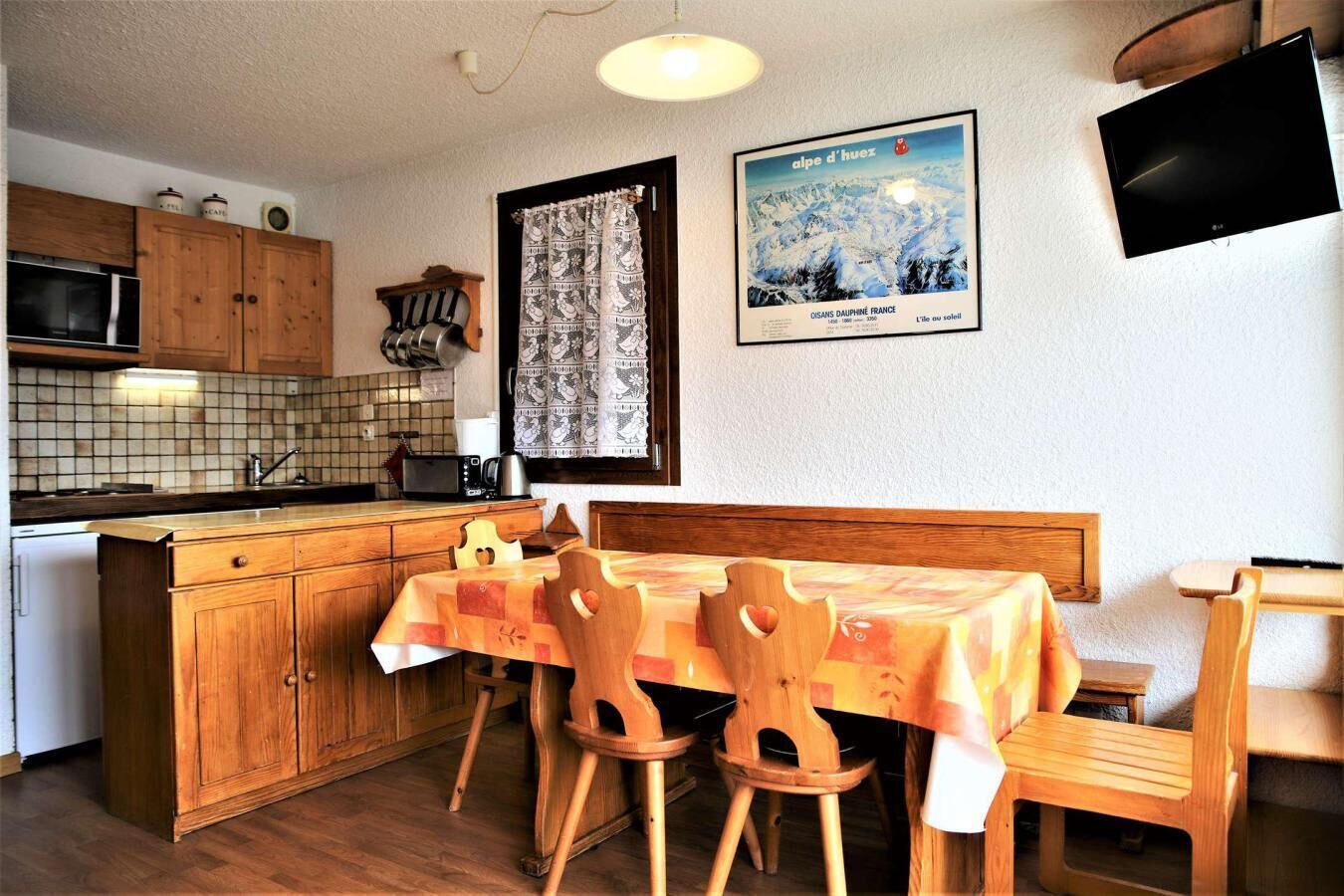 A cozy kitchen with wooden cabinets, a tiled backsplash, a dining table with chairs, and a framed poster on the wall.