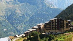 Un edificio de varios pisos con techo plano, rodeado de montañas verdes y un cielo despejado.