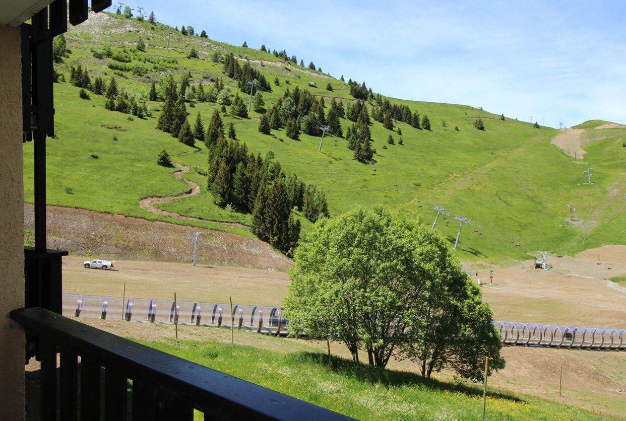 A view of a green hillside with a winding path, a tree, and a fence.