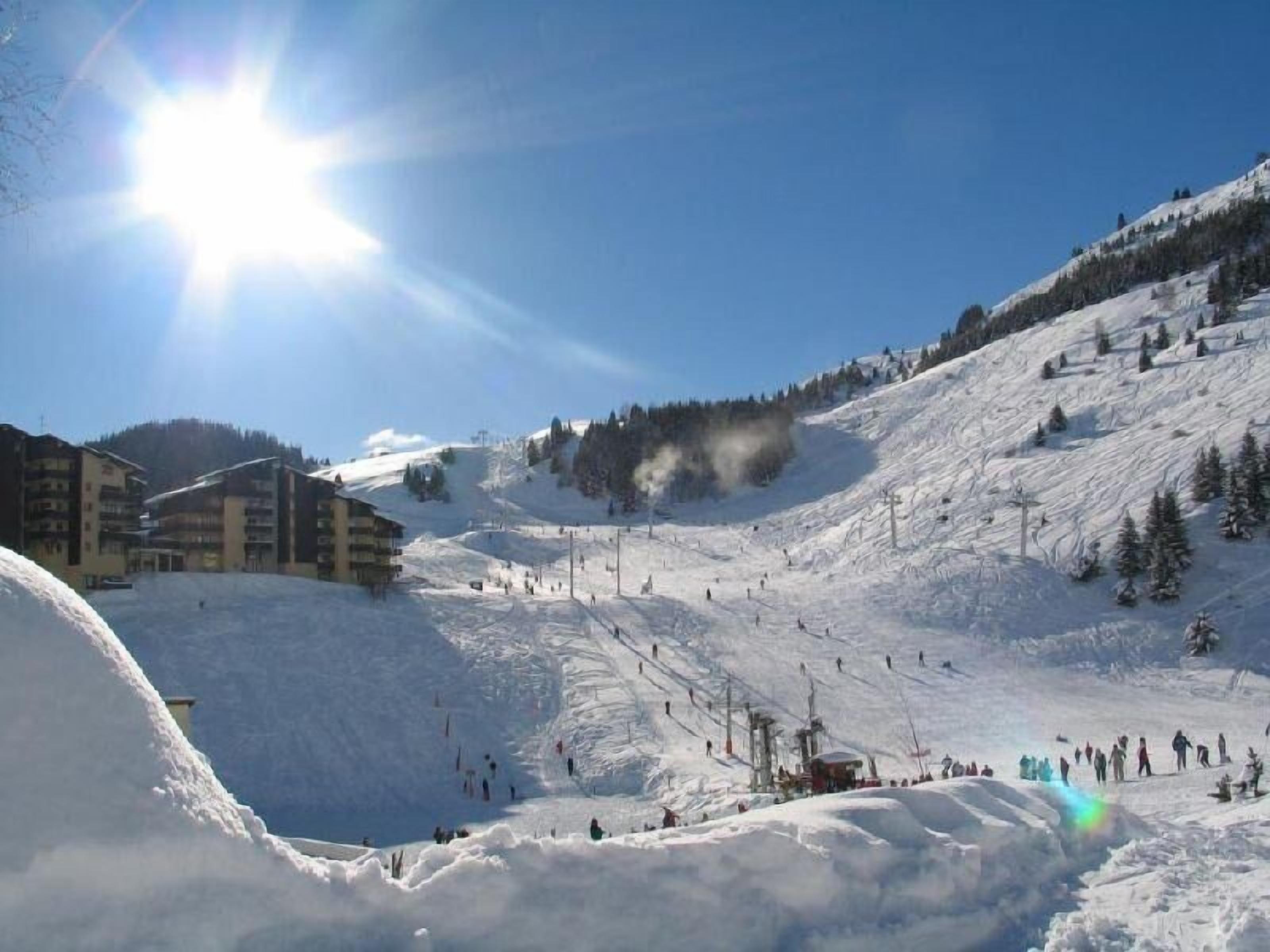 A snowy ski resort with buildings, ski slopes, and a clear sky.