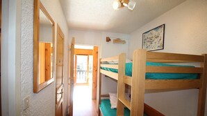 Un pasillo estrecho con literas a la derecha, una puerta de madera a la izquierda y un cuadro en la pared.