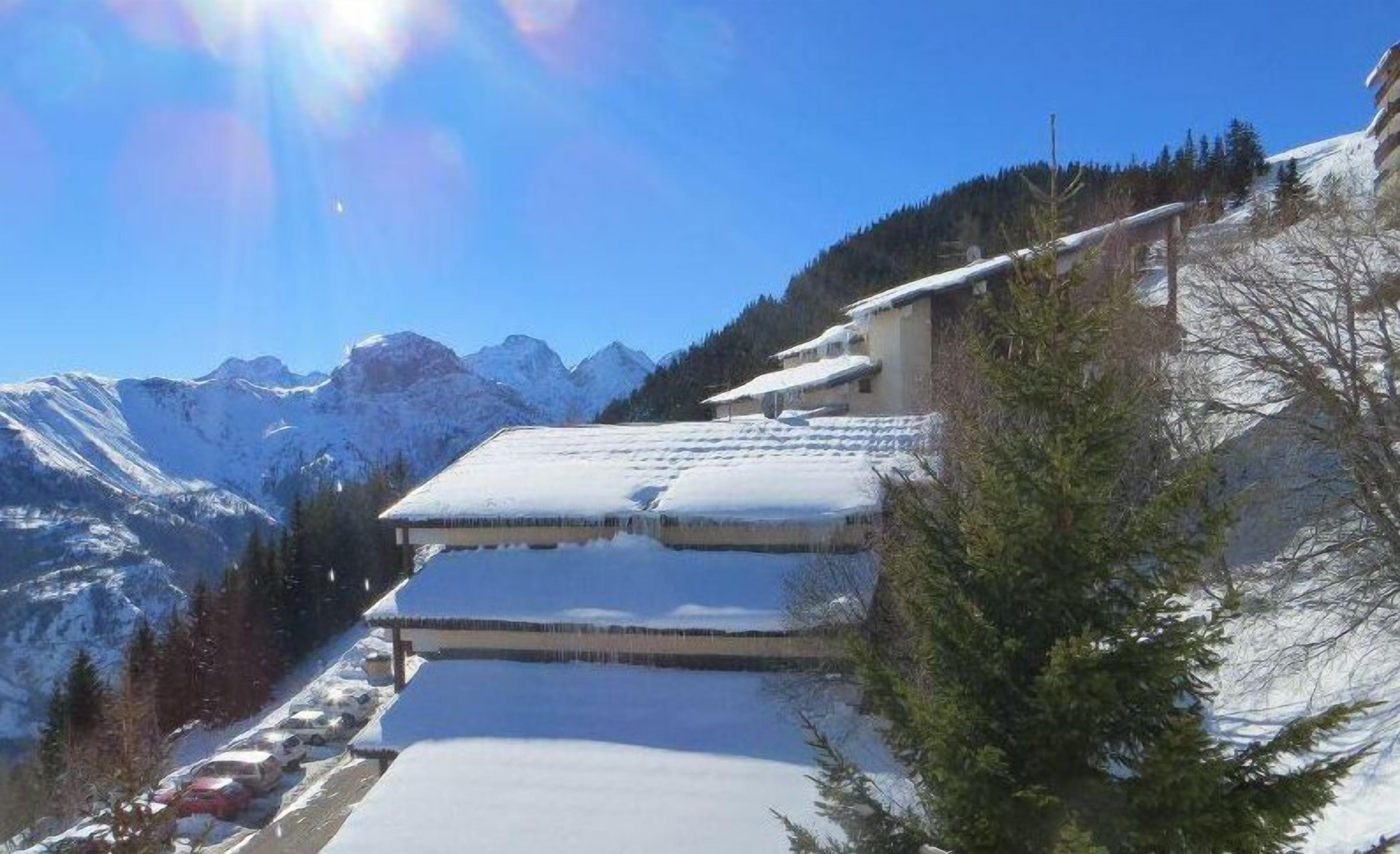 A snow-covered mountain landscape with a building that has a sloped roof, likely a chalet or lodge, situated on a hillside.
