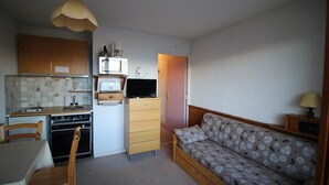 A compact kitchen with a microwave, stove, and sink, a dining table with chairs, and a sofa with patterned cushions. - 300m from resort center, 2nd floor, view mountain, balcony, tv, 17m², Auris en Oisans (Auris)
