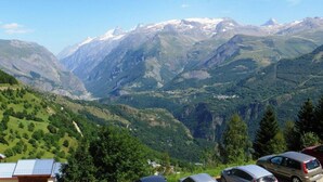 A mountainous landscape with a valley, a few buildings, and parked cars. - 300m from resort center, 2nd floor, view mountain, balcony, tv, 17m², Auris en Oisans (Auris)