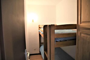 A bunk bed with a headboard against a wall, a small bedside table, and a wall-mounted light. - 10m from ski slopes, 2nd floor, balcony, tv, ski locker, 23m², Auris en Oisans (Auris)