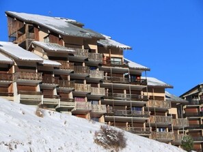 A multi-story wooden building with balconies, likely a hotel or lodge, situated on a snowy slope. - 10m from ski slopes, 2nd floor, balcony, tv, ski locker, 23m², Auris en Oisans (Auris)