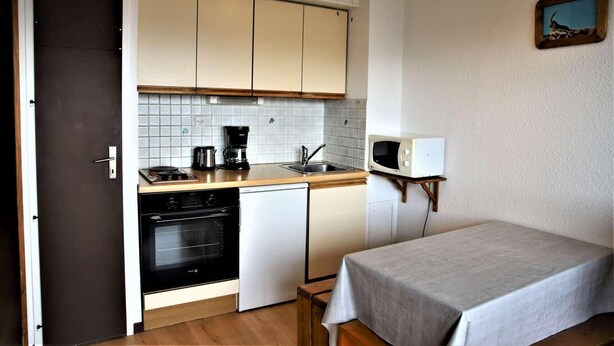 Une cuisine compacte équipée d’un four à micro-ondes, d’une machine à café et d’un four. Une petite table recouverte d’une nappe se trouve dans la pièce.