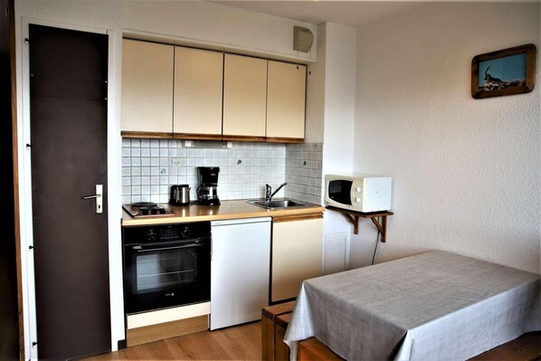 A compact kitchen with a microwave, coffee maker, and oven. A small table with a tablecloth is in the room. - 10m from ski slopes, 2nd floor, balcony, tv, ski locker, 23m², Auris en Oisans (Auris)
