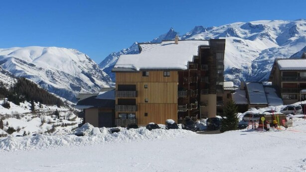 A multi-story building with a wooden facade and a snow-covered roof, surrounded by a snowy landscape and mountains in the background. - 10m from ski slopes, 2nd floor, balcony, tv, ski locker, 23m², Auris en Oisans (Auris)