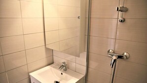 Een badkamer met een witte wastafel, een spiegel en een douche met een handdouche.