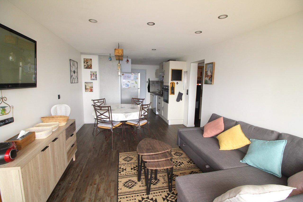 A compact living space with a dining area, kitchenette, and a gray sofa with colorful cushions.
