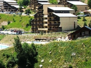 A multi-story hotel with balconies, a swimming pool, and a hilly landscape.