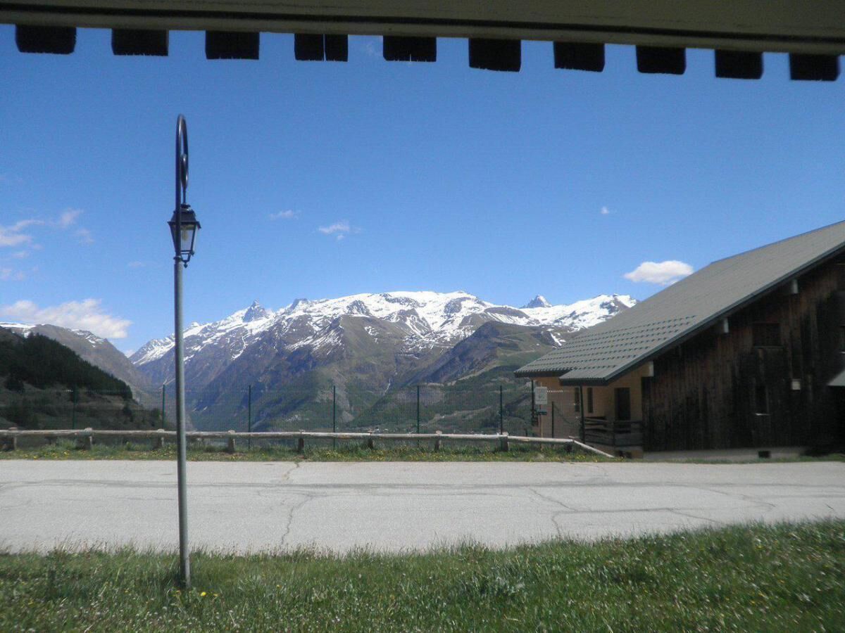 Un bâtiment doté d’un toit en pente et d’une façade en bois, situé dans une zone verdoyante, offrant une vue dégagée sur des montagnes enneigées en arrière-plan.