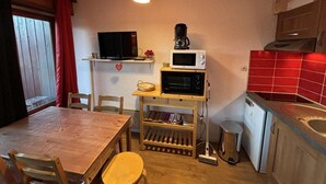 Pieni, käytännöllinen keittiö, jossa on puinen pöytä, tuolit, mikroaaltouuni, kahvinkeitin ja pesuallas.