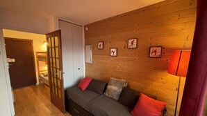 Tunnelmallinen huone, jossa on puuseinä, punaisilla koristetyynyillä varustettu sohva, puuovi ja lamppu.