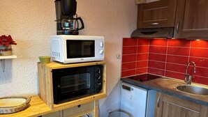 Kompakti keittiö, jossa on mikroaaltouuni, kahvinkeitin ja pieni astianpesukone.