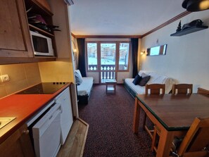 Eine kompakte Küche mit Mikrowelle, Herd und Geschirrspüler. Es gibt einen Essbereich mit Tisch und Stühlen sowie eine Sitzecke mit Sofa. Durch das Fenster ist ein Balkon mit Geländer zu sehen.