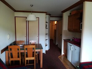 Eine kleine Küche mit Kühlschrank, Mikrowelle und Spüle. Es gibt einen Essbereich mit Tisch und Stühlen.
