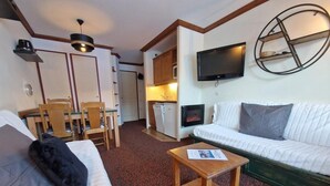 A compact hotel room with a sofa, a small wooden table, a TV mounted on the wall, and a kitchenette in the background. - 50m from ski slopes, 4th floor, view ski slopes, balcony, parking, tv, 29m², La Plagne (La Plagne)