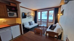 A compact hotel room with a kitchenette, a sofa, a dining table, and a view of a snowy landscape through the window. - 50m from ski slopes, 4th floor, view ski slopes, balcony, parking, tv, 29m², La Plagne (La Plagne)