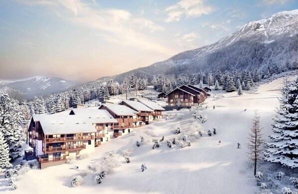 A snow-covered lodge with multiple wooden buildings, surrounded by snow-laden trees and mountains.