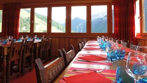 A dining area with a long table set for a meal, wooden chairs, and large windows offering a mountain view. - 100m from ski slopes, balcony, parking, tv, ski locker, 30m², Ceillac en Queyras (Ceillac)