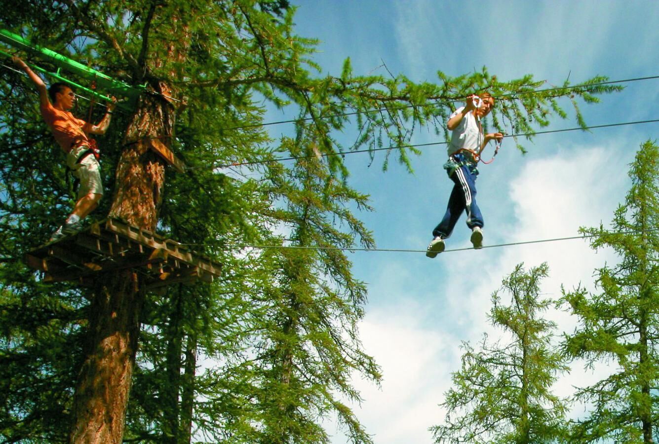 Kaksi henkilöä suorittamassa jonkinlaista toimintaa köydellä, joka on kiinnitettynä puiden välille.